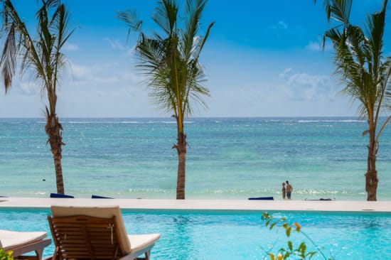 a pool with palm trees and a beach with blue water