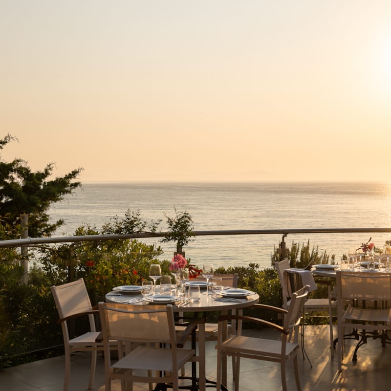 a table set with chairs on a balcony overlooking the ocean