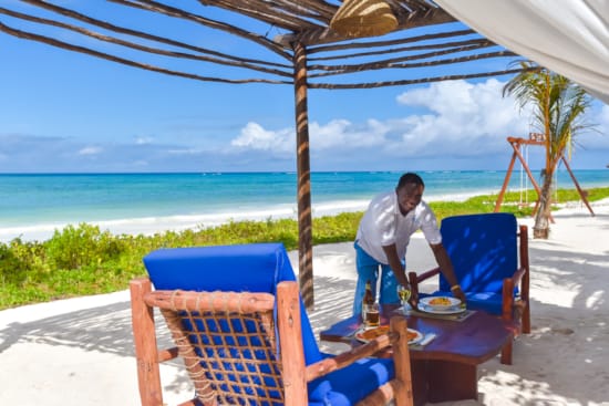a person sitting at a table under a straw umbrella on a beach