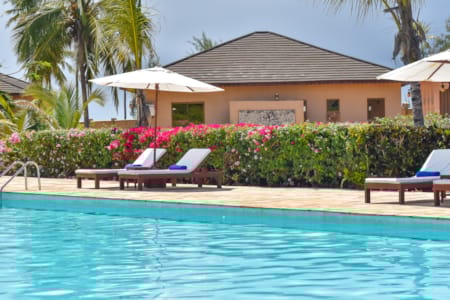 a pool with lounge chairs and umbrellas by a house