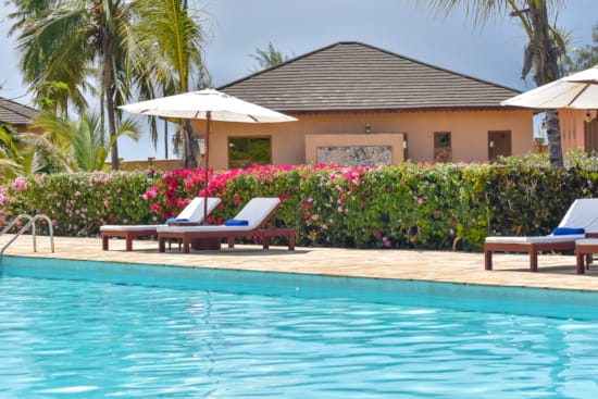 a pool with lounge chairs and umbrellas by a house