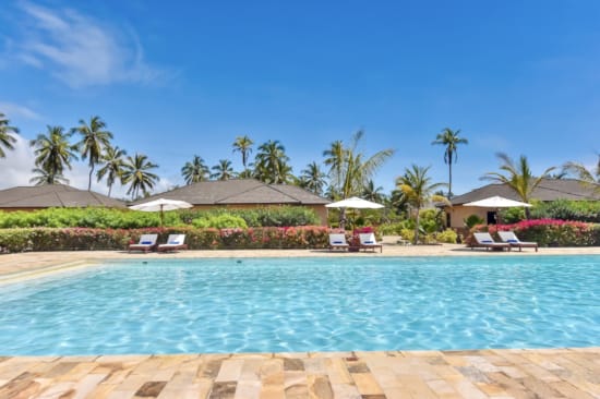 a pool with lounge chairs and umbrellas by a beach