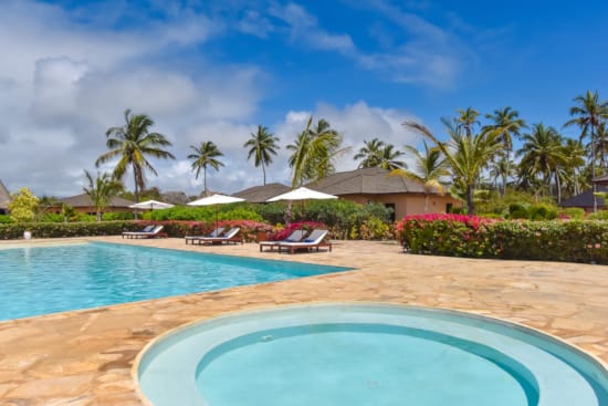 a pool with lounge chairs and umbrellas by a beach