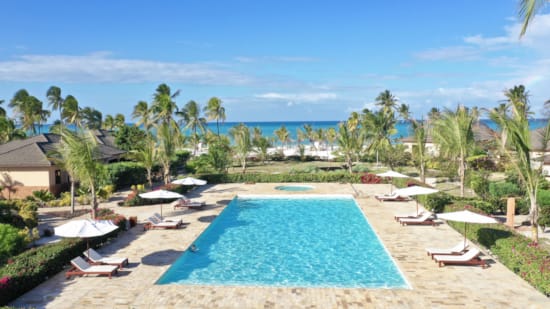 a pool surrounded by lounge chairs and umbrellas on a beach