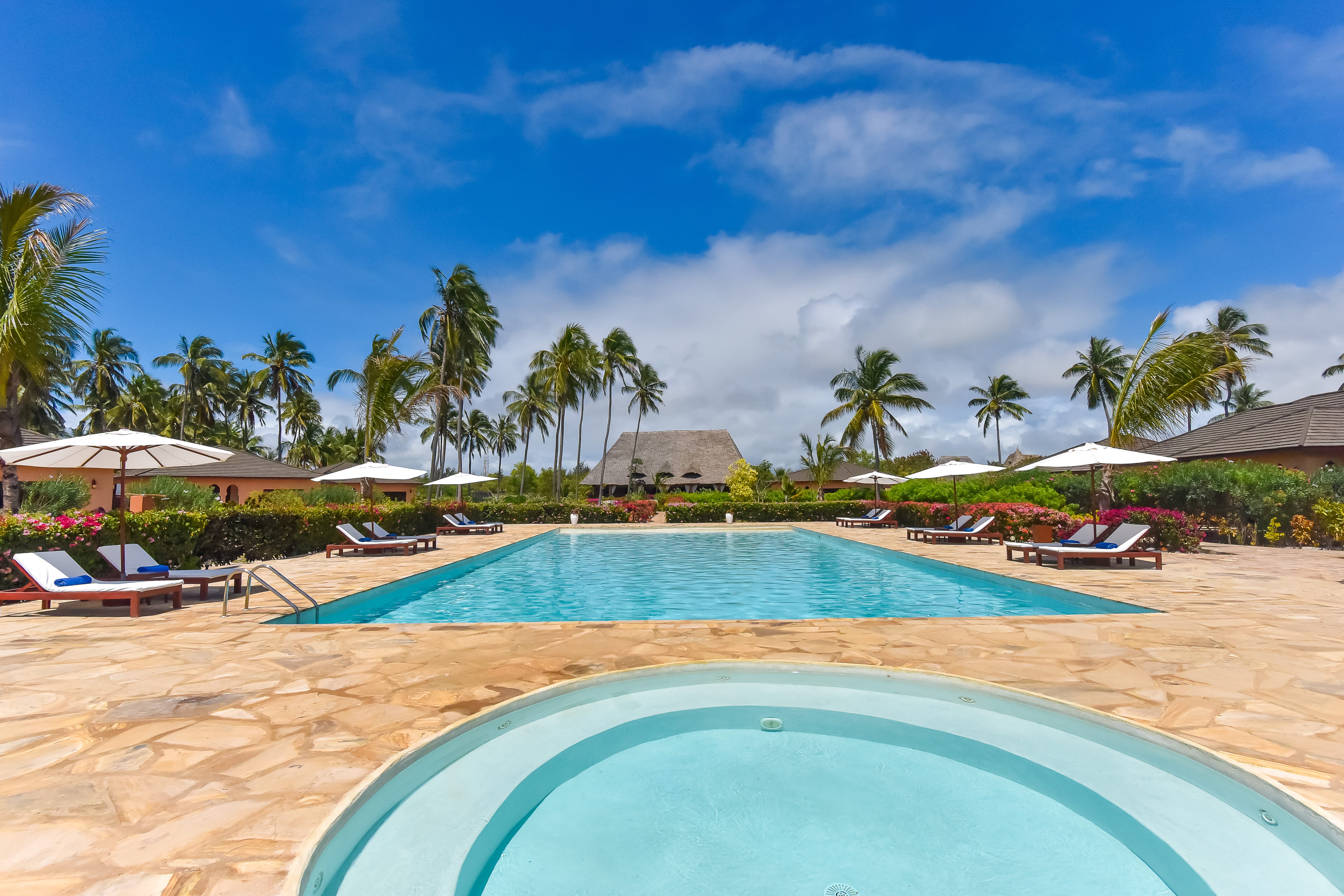 a pool with lounge chairs and umbrellas on a beach