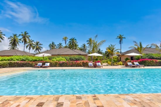 a pool with lounge chairs and umbrellas by a beach