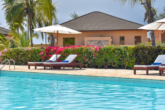 a pool with lounge chairs and umbrellas by a house