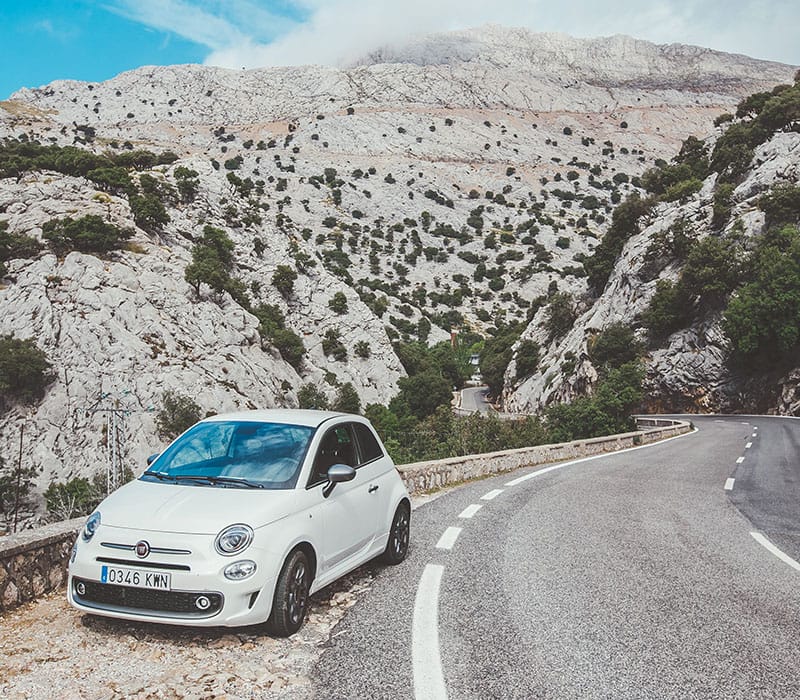 a white car on a road with mountains in the background