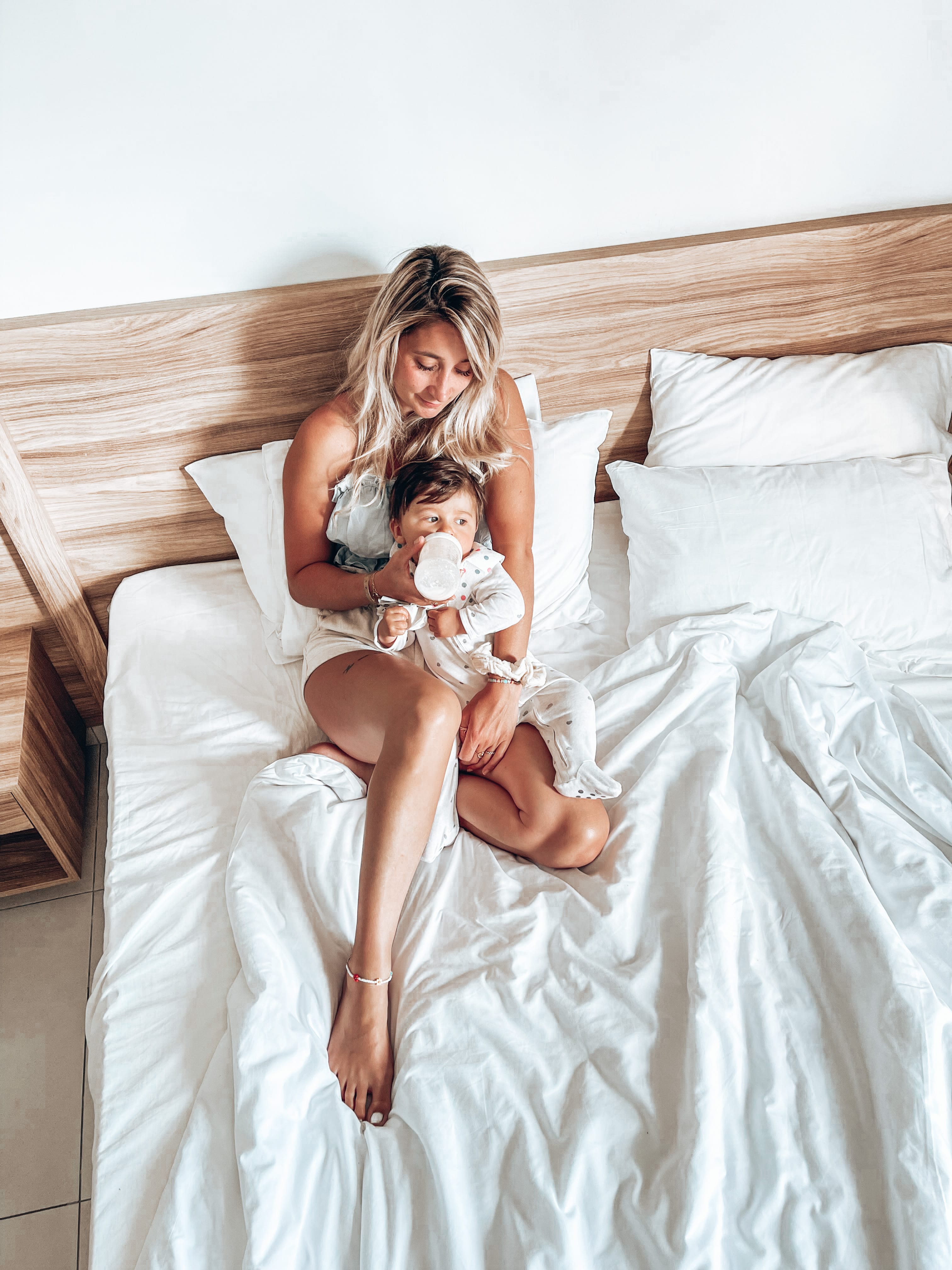 a woman in a white dress sitting on a bed with a baby