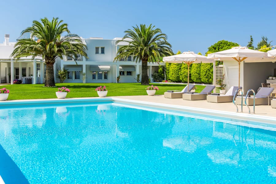 a pool with lounge chairs and umbrellas by a house