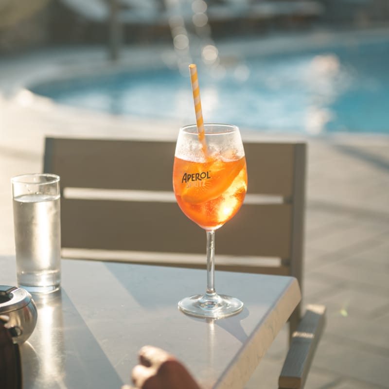 a glass of orange drink on a table by a pool