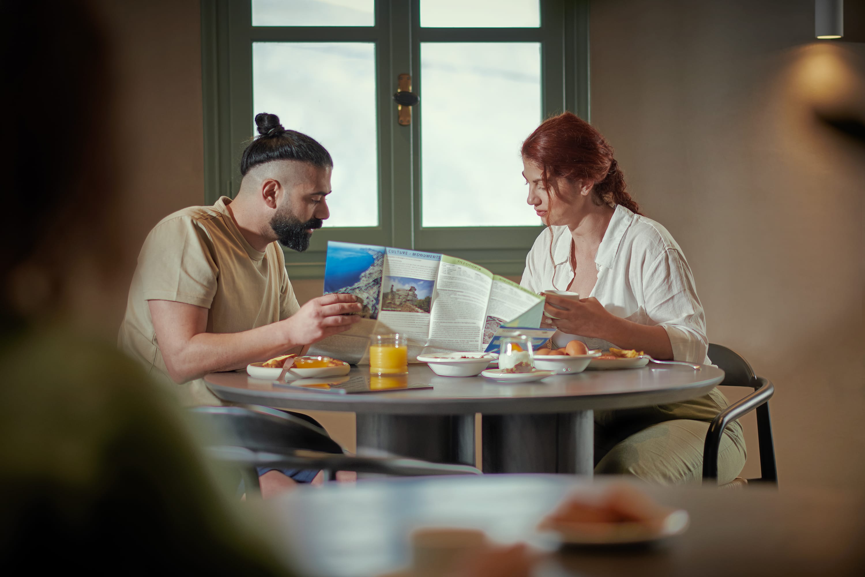 a person and person sitting at a table looking at a magazine