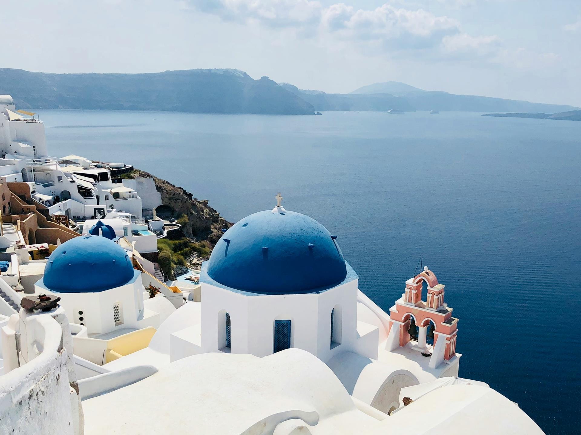 a white building with blue domes and a body of water in the background with Santorini in the background