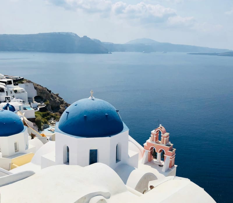a white building with blue domes and a body of water in the background with Santorini in the background