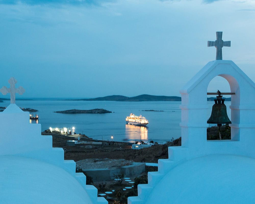 a large white building with a cross on top and a body of water in the background