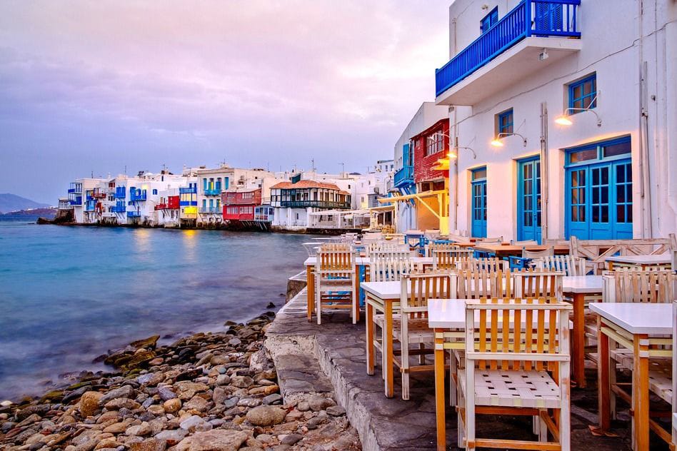 a row of tables and chairs on a rocky beach with buildings in the background