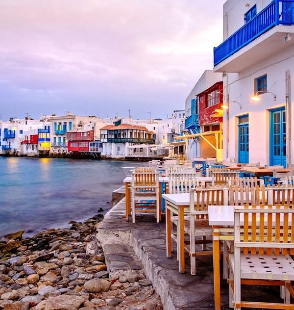 a row of tables and chairs on a rocky beach with buildings in the background