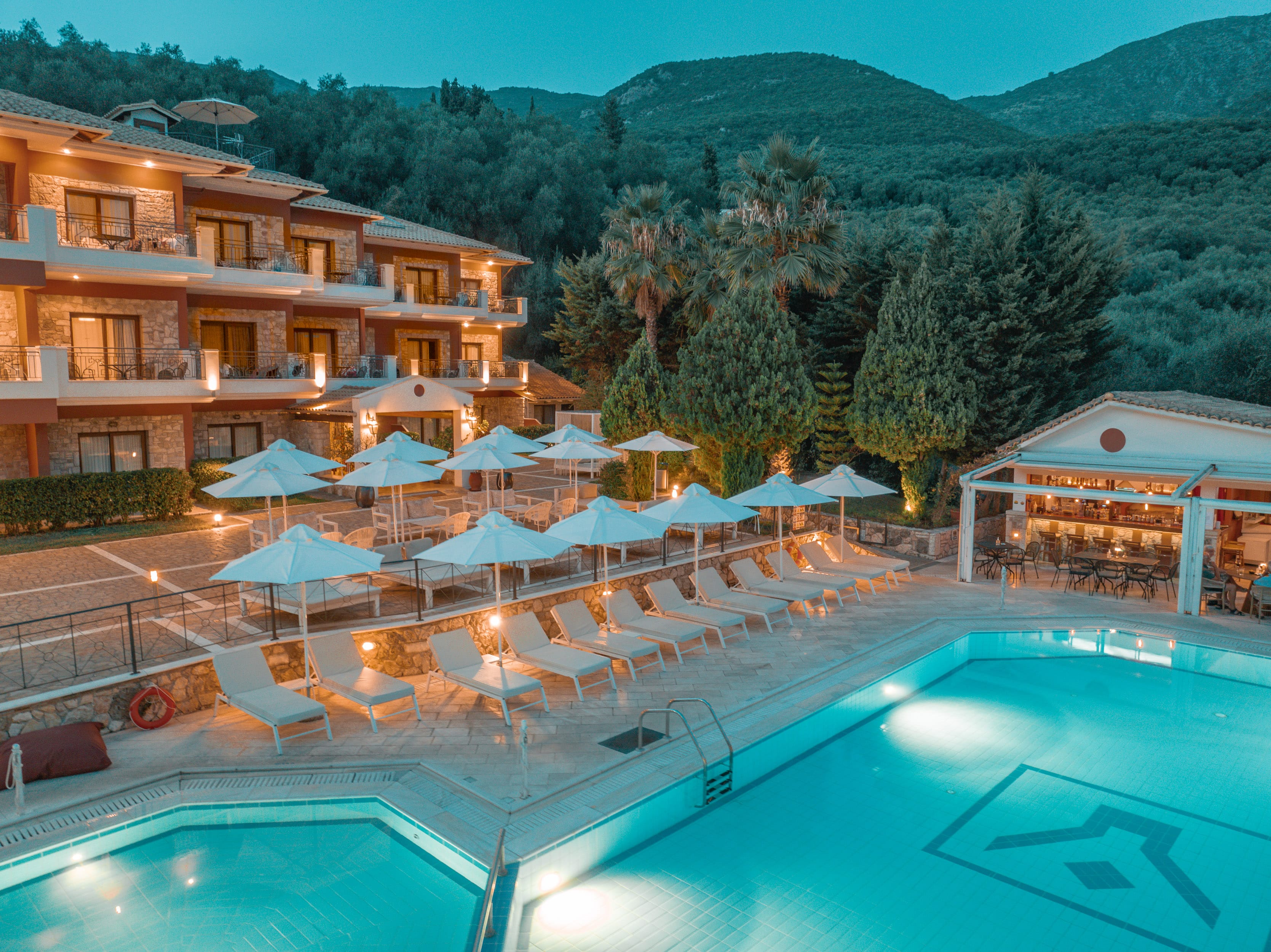 a pool with umbrellas and chairs by a building with trees in the background