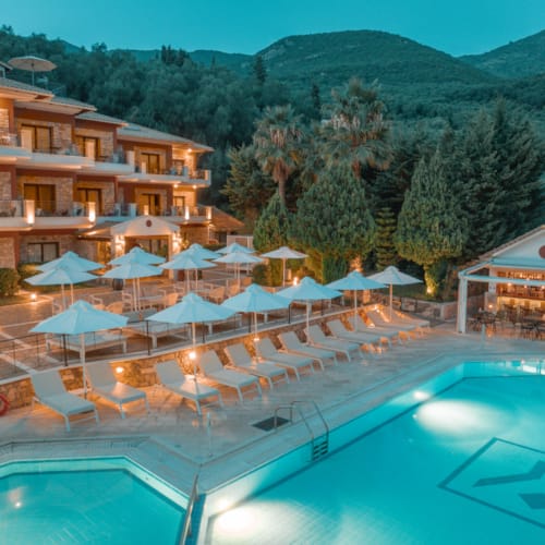 a pool with umbrellas and chairs by a building with trees in the background