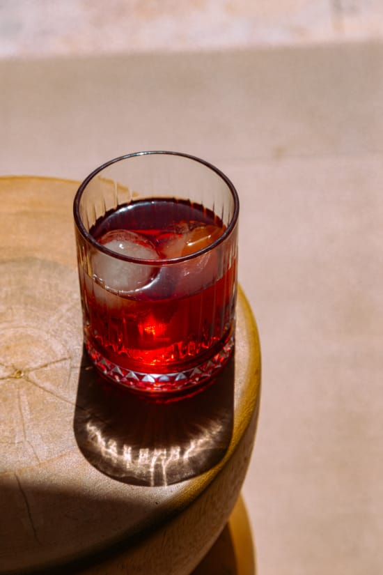 a glass of red liquid with ice on a wood surface