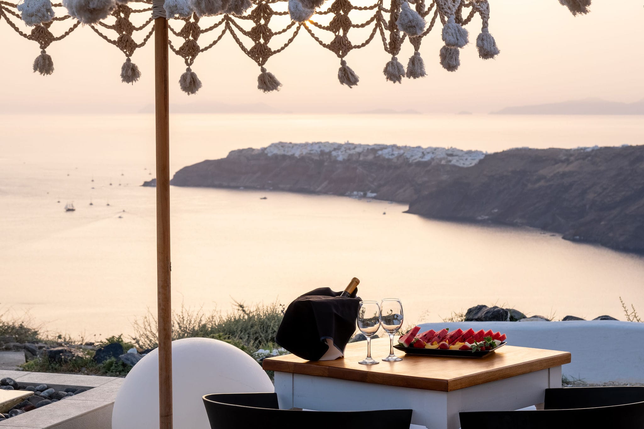 a table with a plate of food and glasses on it by a body of water
