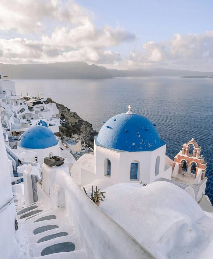 a white building with blue domes and a blue dome on a cliff above water