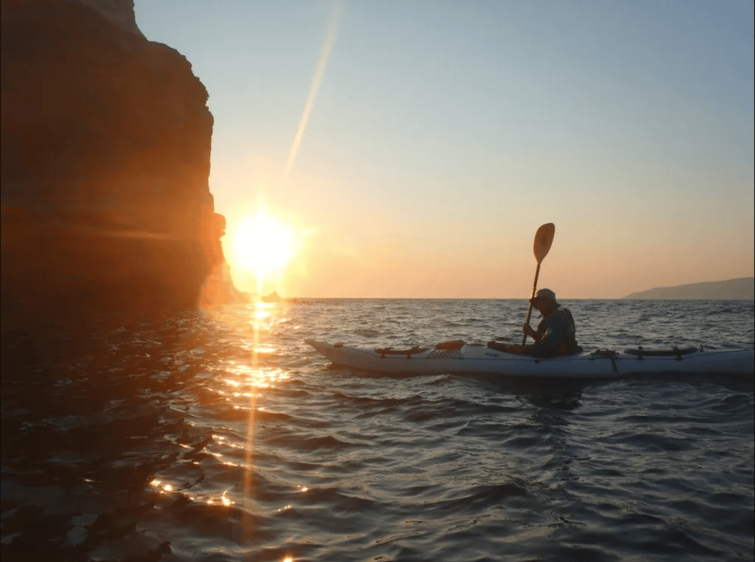 a person in a kayak in the water with the sun setting