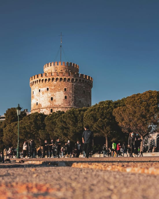 a group of people standing in front of a castle with White Tower of Thessaloniki in the background