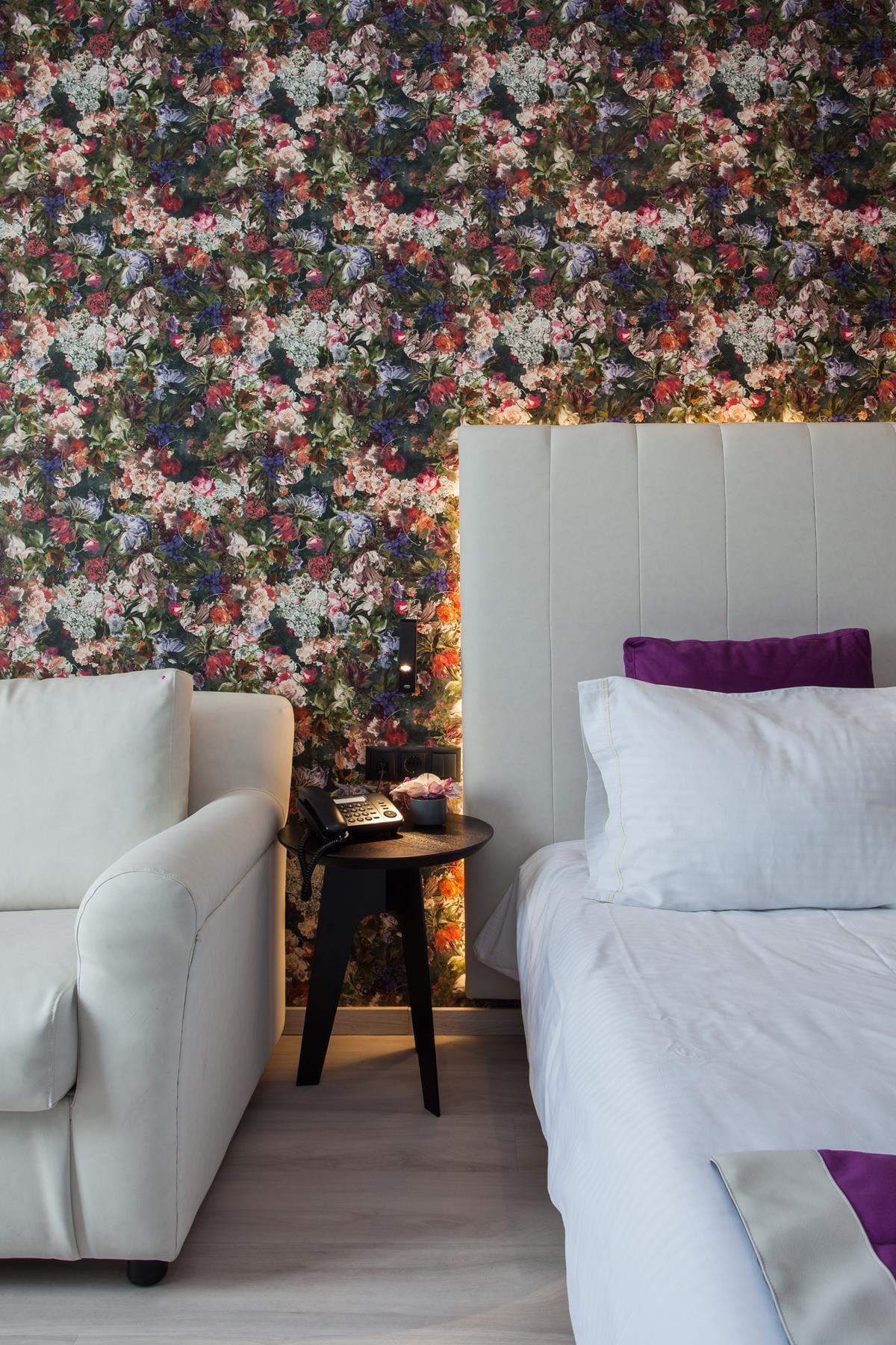 a room with a bed and a table with a flowered wallpaper