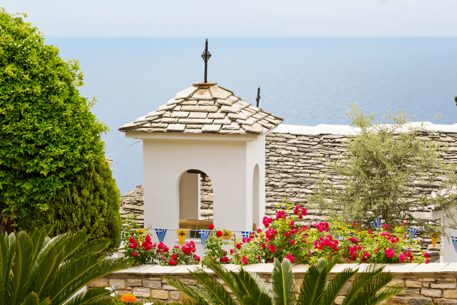 a white building with a cross on top and a hill with flowers