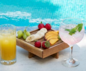 a plate of fruit and a glass of juice by a pool
