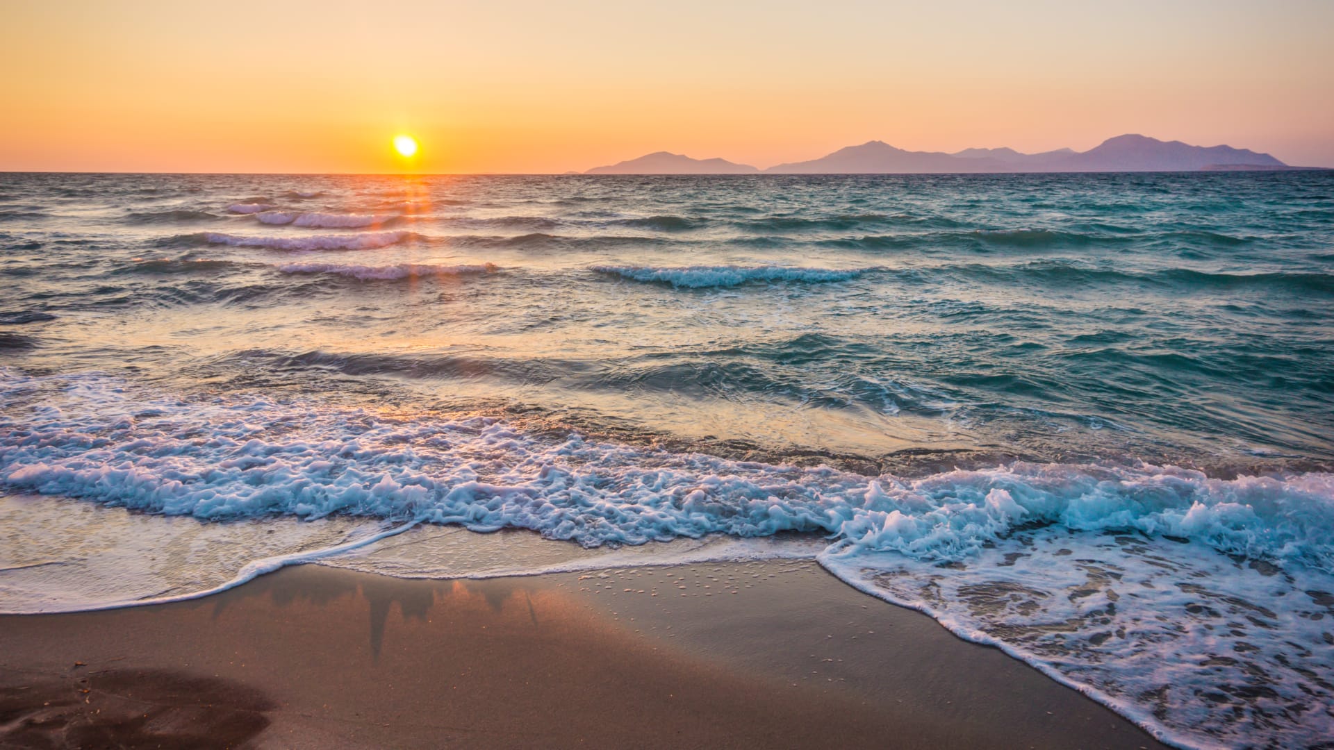 a beach with waves and the sun setting