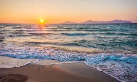a beach with waves and the sun setting