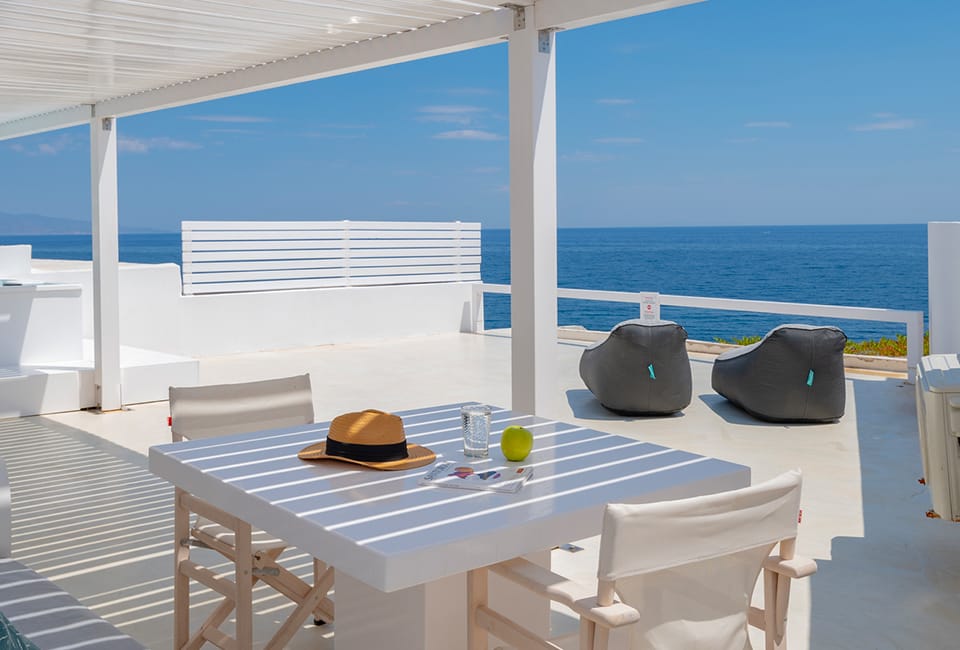 a table with a hat and chairs on a deck with a body of water in the background
