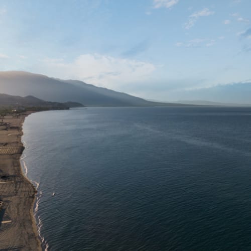 a body of water with a beach and mountains in the background