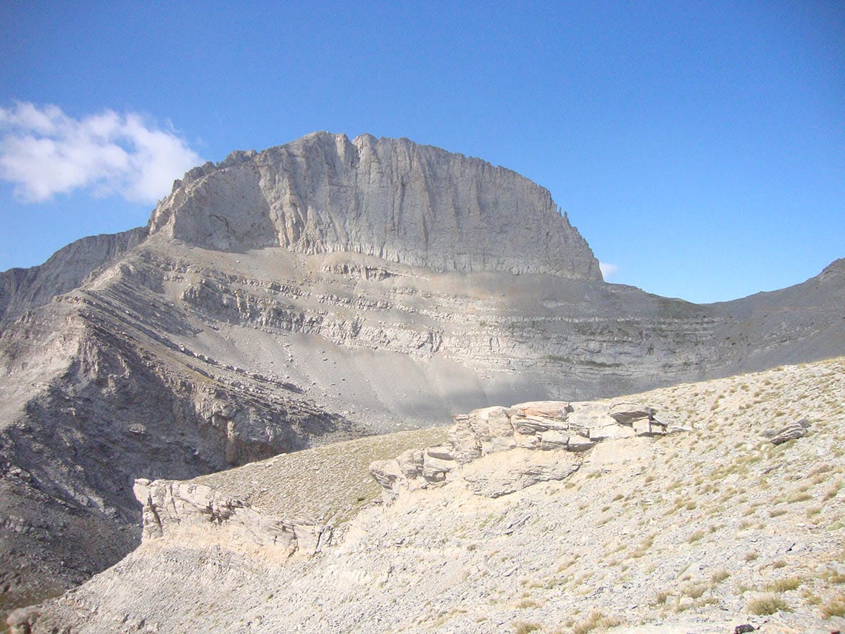 a rocky mountain with a valley below with Mount Olympus in the background
