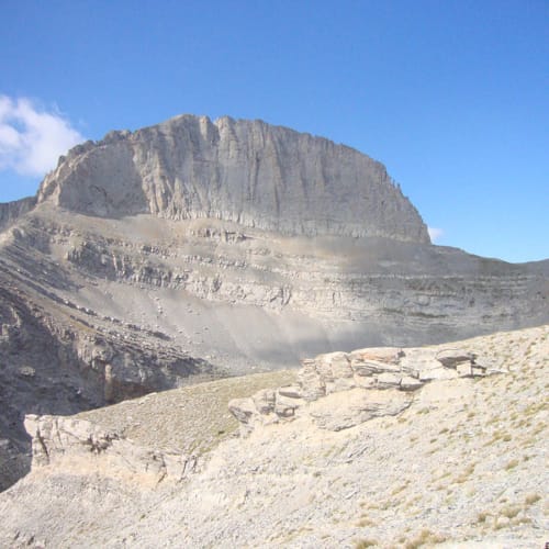 a rocky mountain with a valley below with Mount Olympus in the background