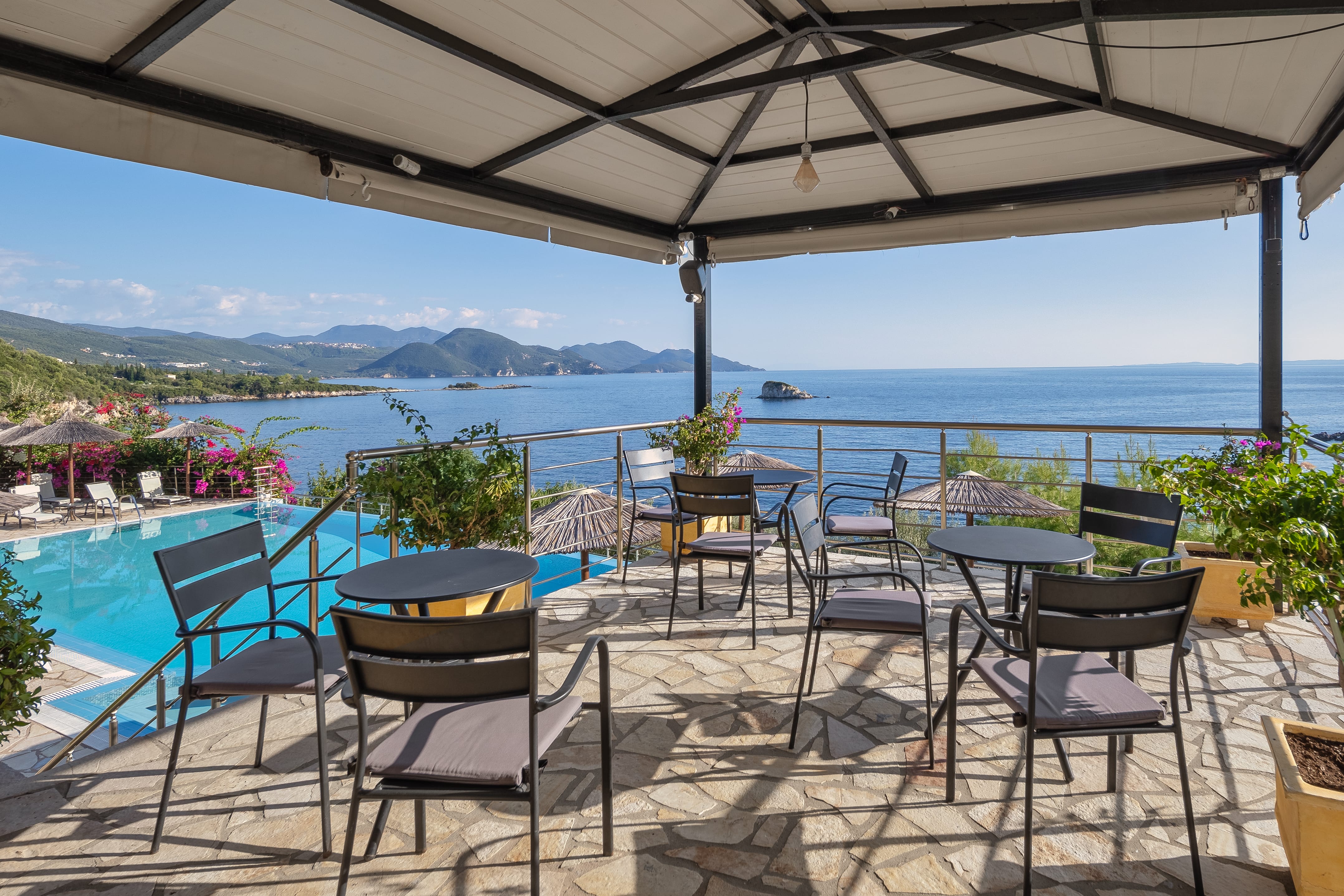 a patio with tables and chairs and a body of water in the background