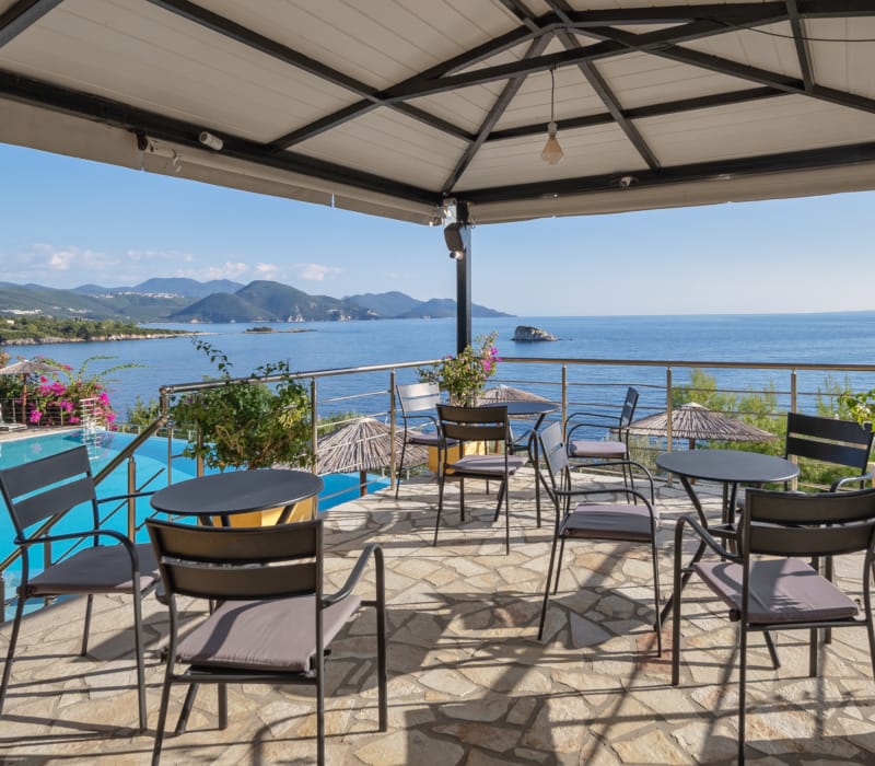 a patio with tables and chairs and a body of water in the background