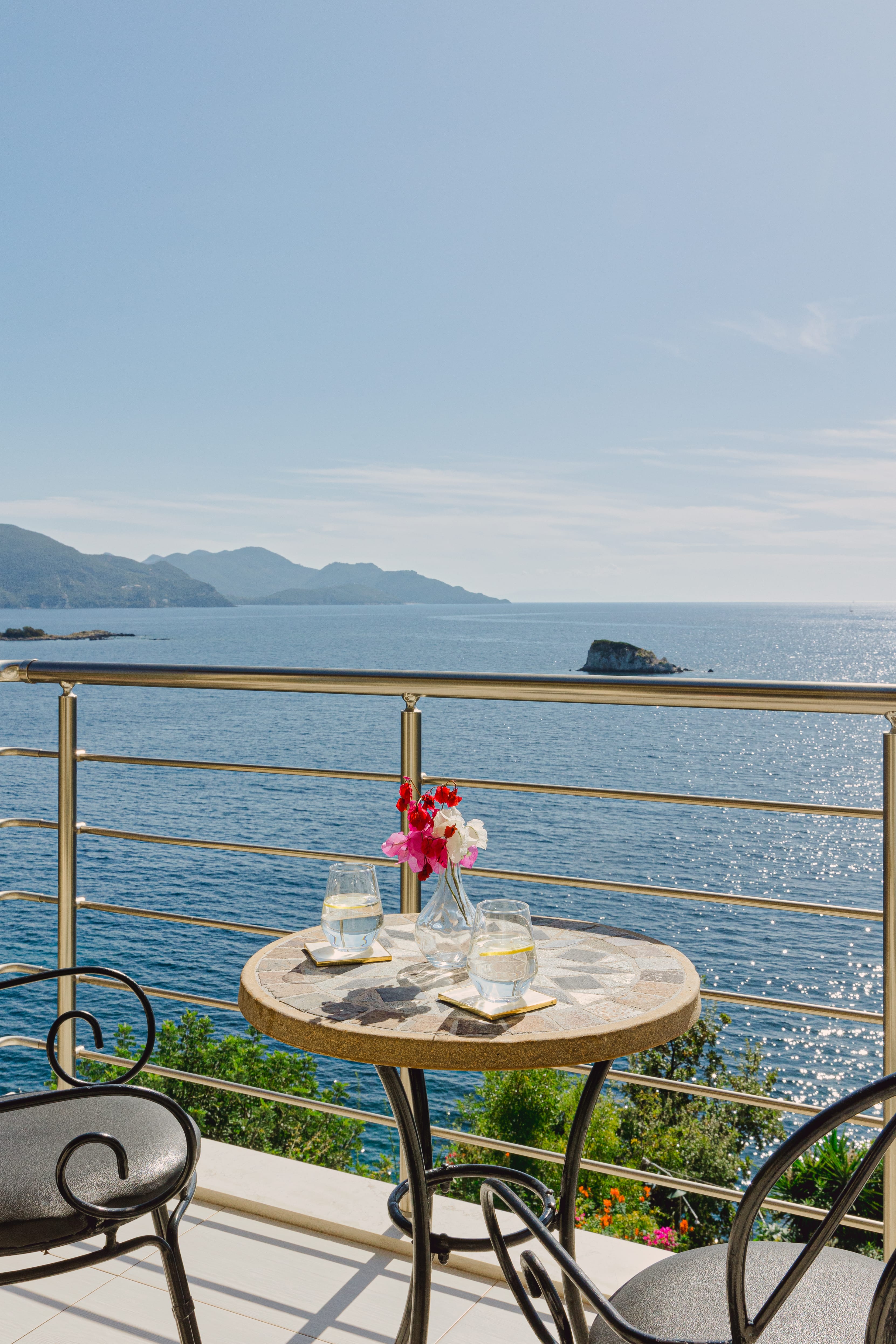 a table with glasses and flowers on it by a body of water