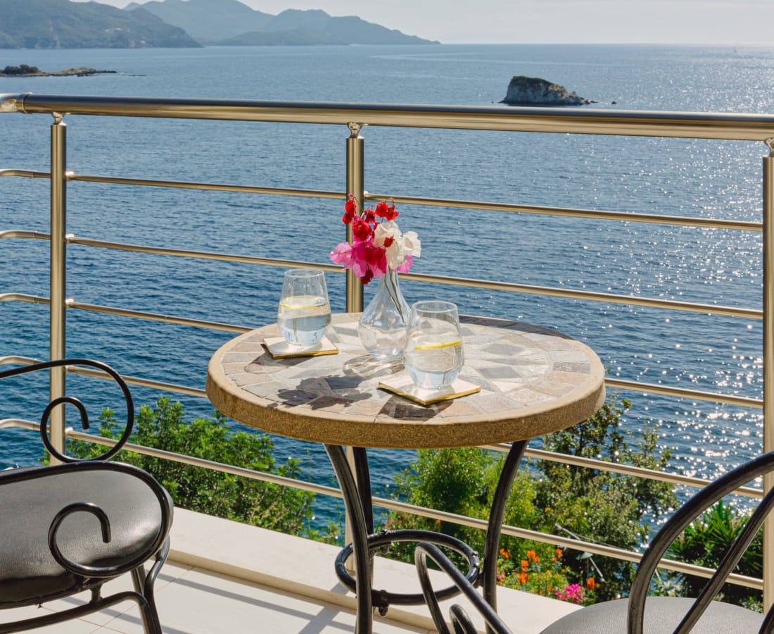 a table with glasses and flowers on it by a body of water