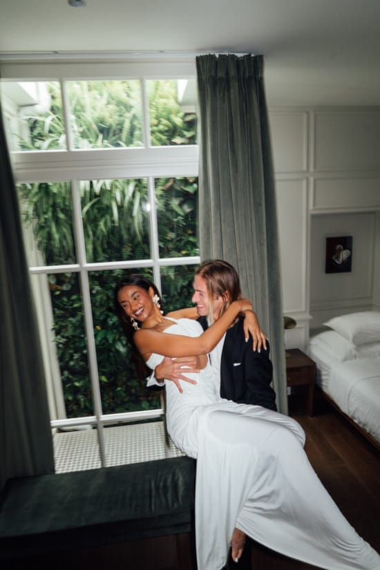 a man and woman hugging in a room with a window and curtains
