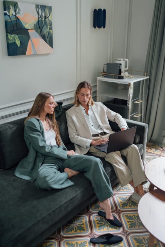 a couple of women sitting on a couch looking at a laptop