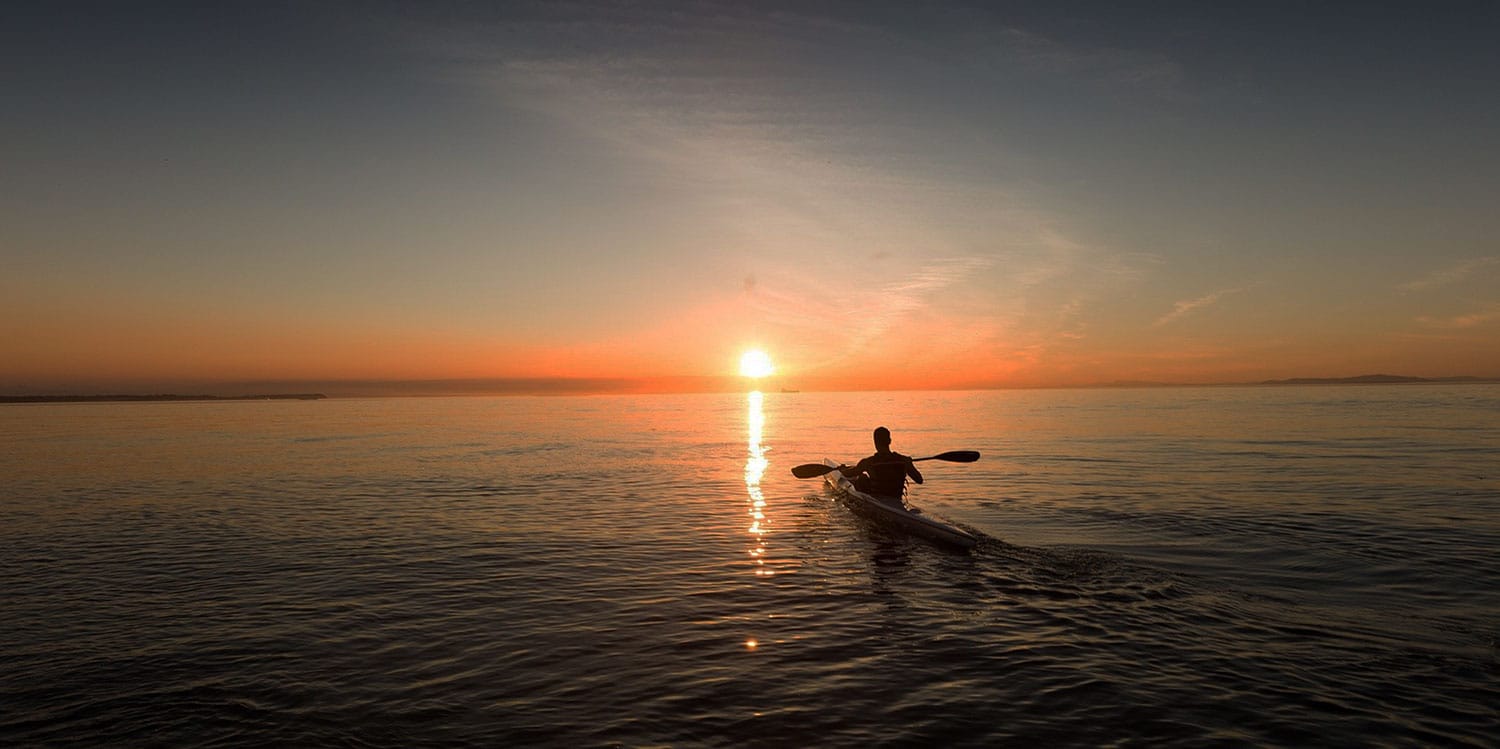 a person in a boat in the water with the sun setting
