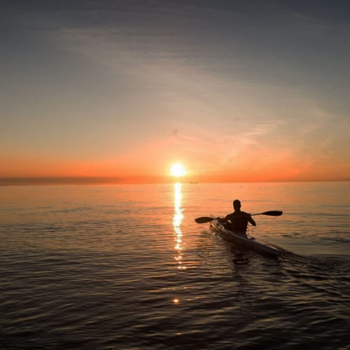 a person in a boat in the water with the sun setting