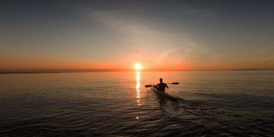 a person in a boat in the water with the sun setting