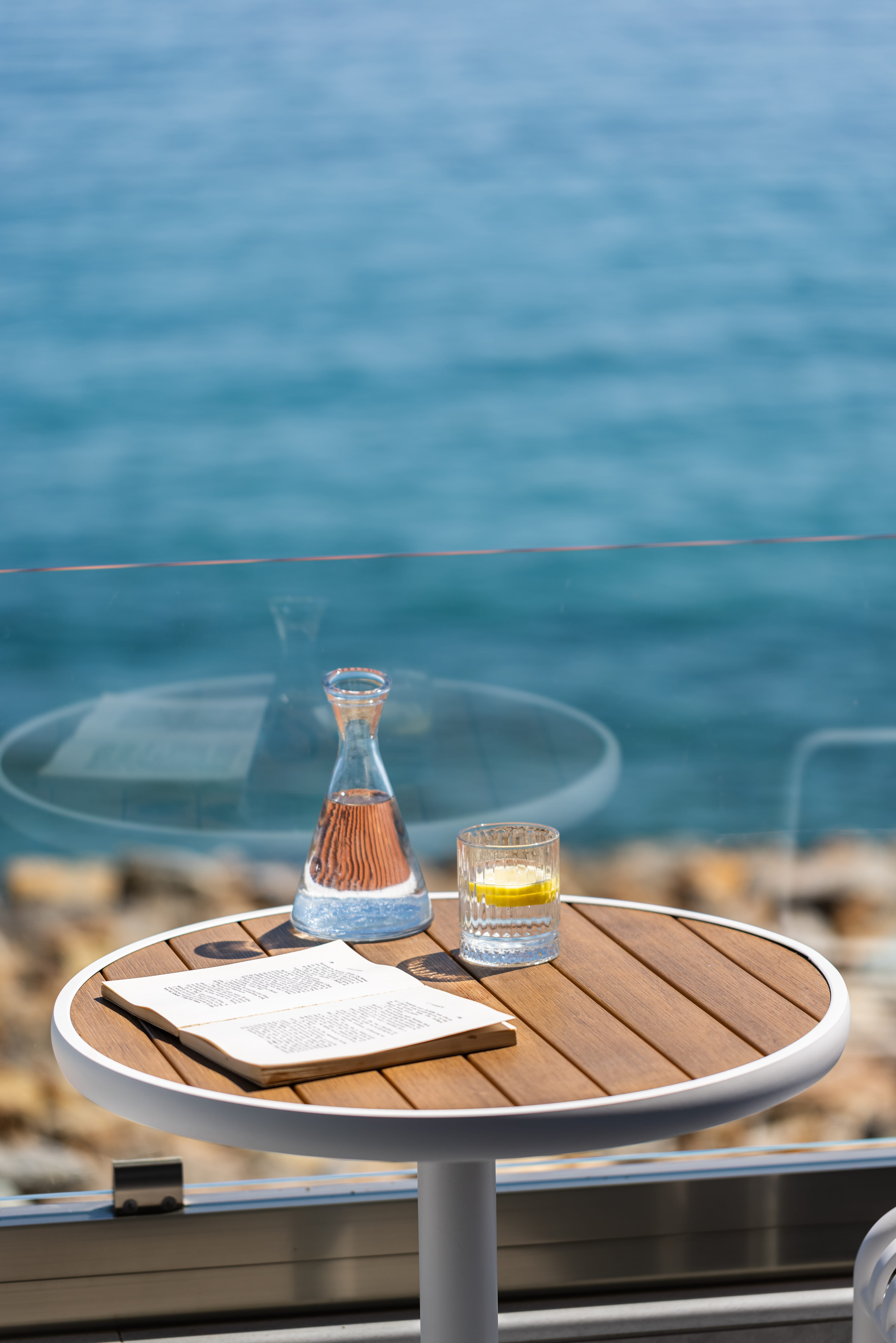 a table with a glass bottle and a glass of liquid on it by a body of water