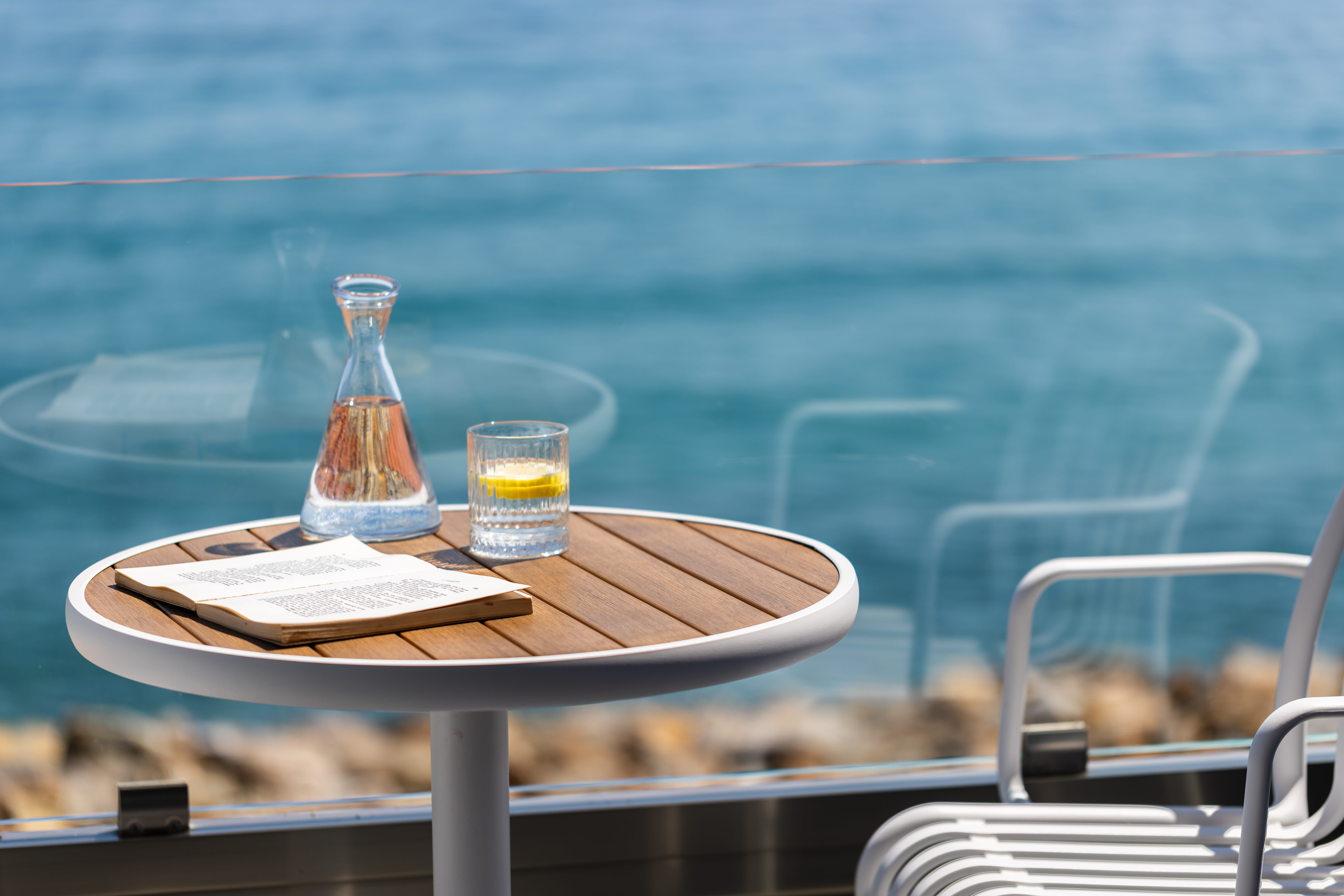 a table with glasses and a bottle of alcohol on it by a body of water