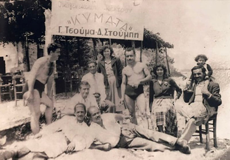 A black-and-white family photo of the owners of KYMATA Restaurant in front of the old sign that reads “Oikogeneikon Kentron Kymata.”