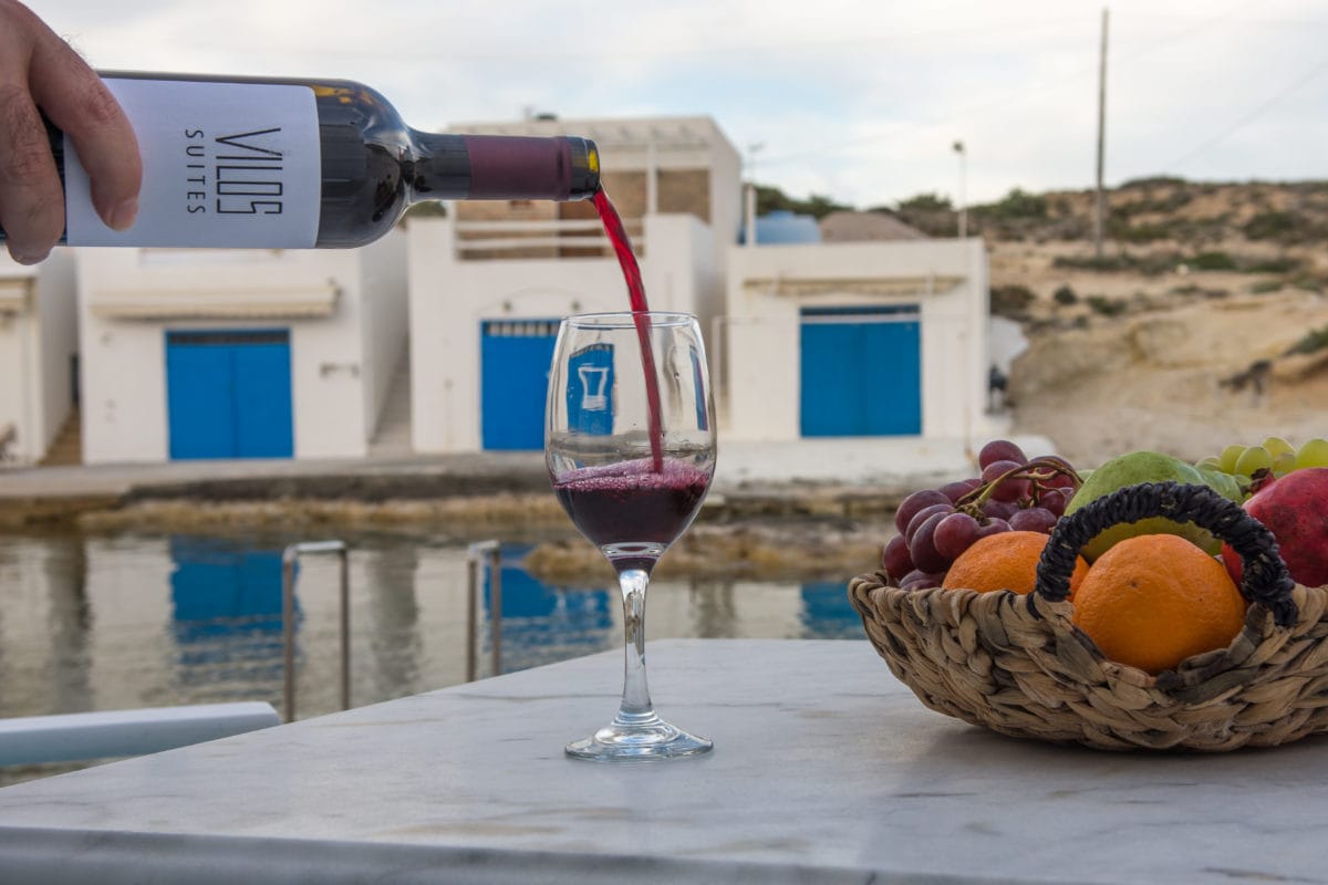 a glass of wine next to a bottle of wine and a basket of fruit